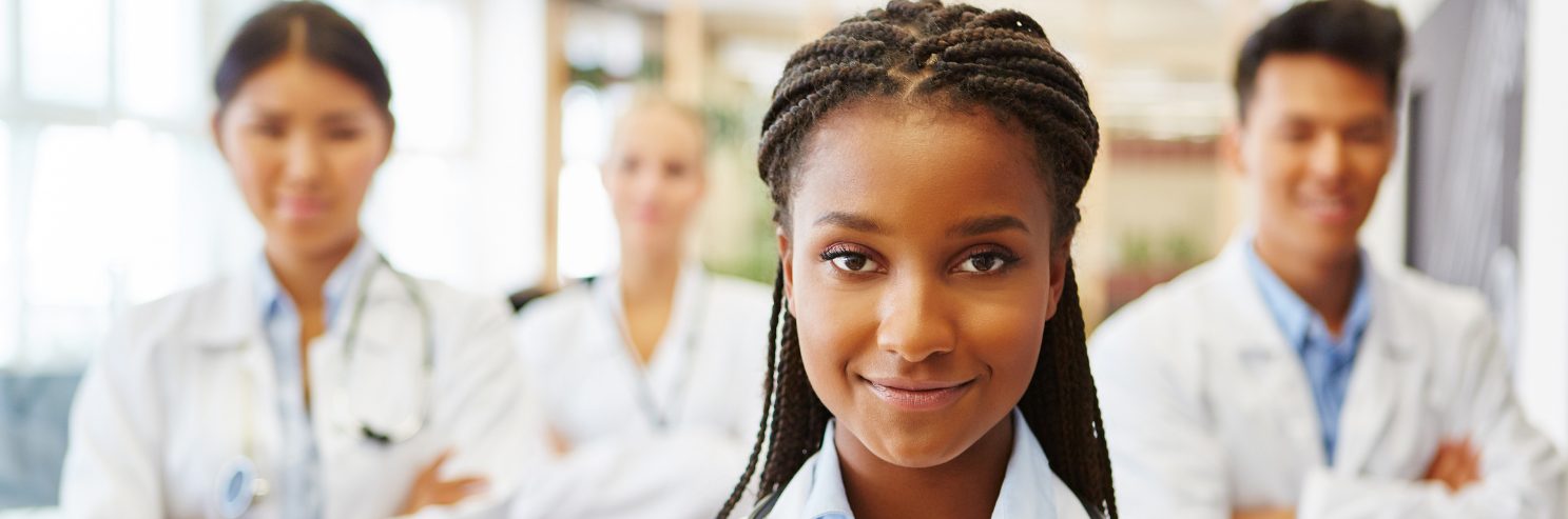 A smiling young healthcare worker standing with her clinical team in a bright medical facility