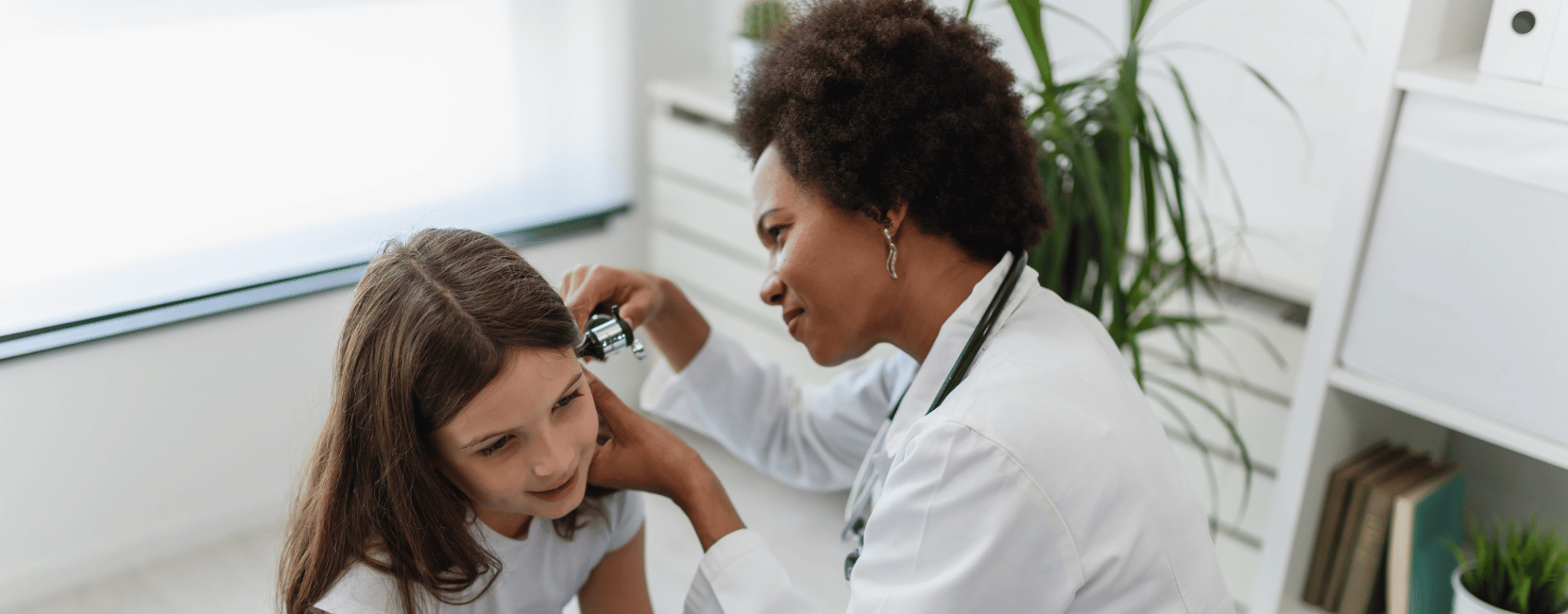 A licensed vocational nurse in a white coat examining a young patient's ear during a clinical visit